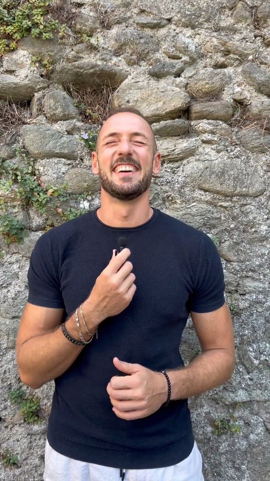 Stefano ride davanti a un muro di pietra del borgo